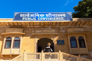 a aged man is sitting in front of public toilet at jaisalmer.