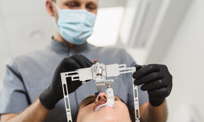 An experienced dentist placing a facial bow for woman patient to examine the bite. Modern technologies in dental treatment