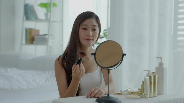 A beautiful Asian woman sitting in the mirror with her makeup in a good mood in the morning.Her pet a dog pug come into troubler the makeup table. Healthy skin care and cosmetic concept