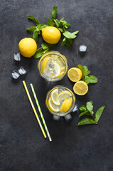 Cold lemonade with mint and ice on a black concrete background, top view.