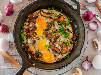 Overhead view of Fried eggs with mushroomes and red onions in a cast iron pan