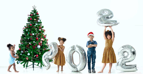 Children of different color and races have fun with metallic silver number balloons and Christmas trees, a diverse group of children, including African and asian, 2022 Happy new year, white background