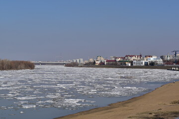 Fototapeta na wymiar Spring city landscape. Early spring, ice drift on the river. View from the shore of the ice drift and the city.