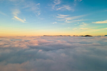 Fototapeta na wymiar Aerial view of vibrant sunset over white dense clouds with distant dark mountains on horizon.