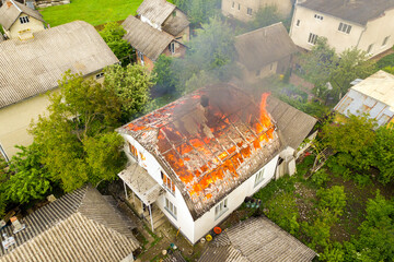 Aerial view of a house on fire with orange flames and white thick smoke.