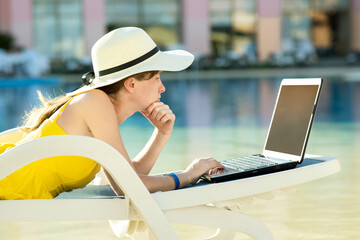 Young woman on beach chair at swimming pool working on computer laptop connected to wireless...
