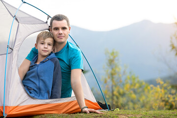 Young father with his child son resting together in a hiker tent in summer mountains. Active family recreation concept.