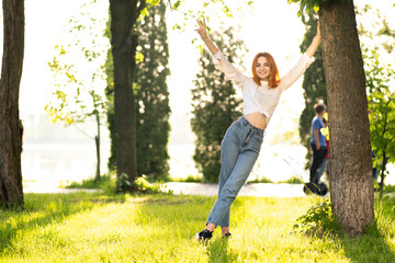Young positive redhead woman in casual clothes enjoying warm day in summer park .