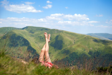 Young woman in red dress lying down on green grassy field resting on a sunny day in summer mountains enjoying view of nature.