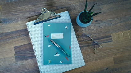 Notebook with Pen and Glasses on wooden Desk