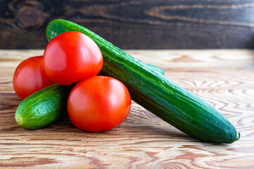 two cucumbers and three tomatoes on a wooden background