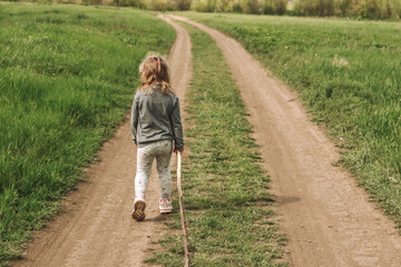 The child plays with a tree stick. Children's portrait. Blonde Girl 4 years old. Human and nature. The baby is playing in nature.