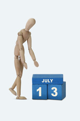 day of the month 13 July calendar . A calendar date on blue cubes and a wooden man standing next to it. White background
