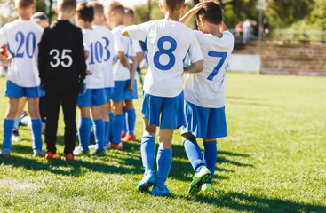 Obraz premium Boys in School Sports Team on the Field. Kids in a Group With Soccer Coach. Children Playing Football Match. Game Break in a Football Match