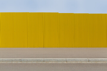 Bright yellow corrugated iron on a sidewalk with blue sky