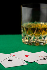 Close-up of poker cards on green tablecloth with glass of whiskey, defocused, black background, vertical, with copy space