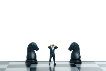 Businessman using binoculars standing in between horse knight chess pawn. Miniature tiny people...