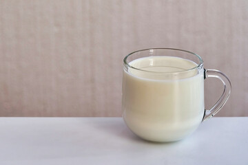 Transparent glass mug with milk on white table
