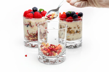 Muesli with yogurt and berries in a glass On a white background. Muesli is poured from a spoon into a glass. Dessert preparation process. Healthy breakfast. Fitness food. High quality photo
