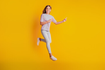 Fototapeta na wymiar Photo of jumping running high schoolgirl point finger empty space isolated on yellow background