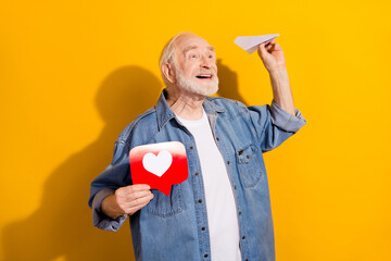 Portrait of attractive cheerful man holding like sign throwing paper plane isolated over vivid yellow color background