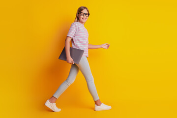 Fototapeta na wymiar Photo of clever kid girl walk with laptop isolated over yellow background