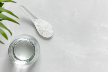 Collagen powder in a spoon and a glass of water on a gray concrete background with a copy space. Extra protein intake