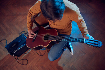 Male musician playing acoustic guitar on the amplifier in retro vintage room.