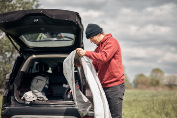 Camper packing and unpacking from a car's roof rack in nature.