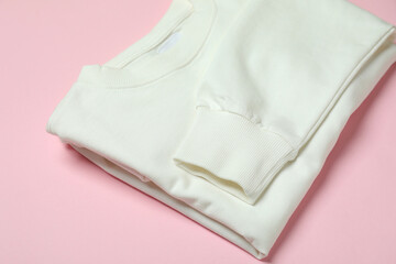 Folded white sweatshirt on pink background, close up