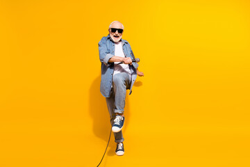 Full length body size of grandfather in sunglass dancing keeping microphone on festival isolated vibrant yellow color background