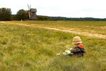 little boy in straw hat drawing in a field. Autumn countryside