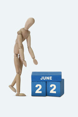 day of the month 22 June calendar . A calendar date on blue cubes and a wooden man standing next to it. White background