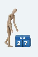 day of the month 27 June calendar . A calendar date on blue cubes and a wooden man standing next to it. White background