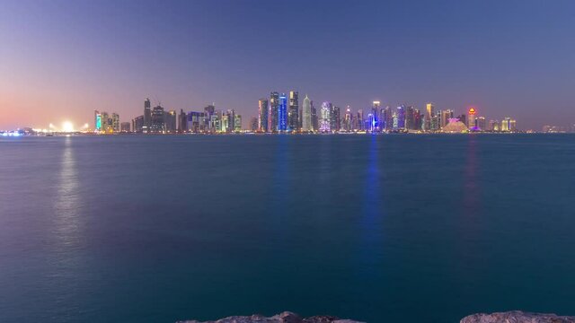 Doha downtown skyline day to night transition timelapse, Qatar, Middle East. Illuminated skyscrapers on a West Bay reflected in a water of Gulf