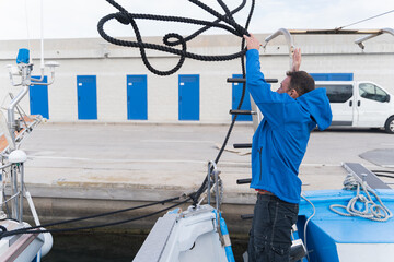 Man throwing a rope from a ship moored in a harbour.