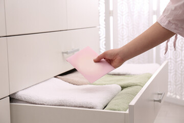 Woman putting scented sachet into drawer with towels, closeup