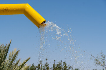 Water falling from bright colored yellow fountain to pool below. Copy space right.