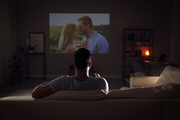 Man watching movie on sofa at night, back view
