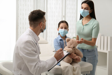 Mother with daughter visiting pediatrician in hospital. Wearing protective masks