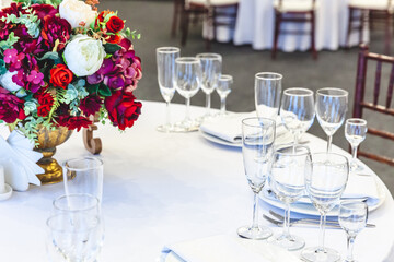 Fancy table set for dinner with flower composition in restaurant, luxury interior background. Wedding elegant banquet decoration and items for food arranged by catering service on white table.