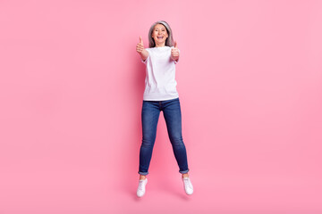 Full length body size photo of woman jumping up showing thumb-up sign isolated pastel pink color...