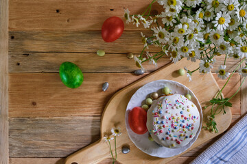 Easter cake with colored eggs and wild chamomiles on the old wooden table