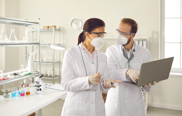 Diverse scientist, scientific researcher or doctor in facial mask discuss test result using laptop...