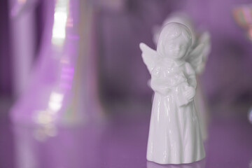 Small white marble figurine of an angel in dress on a light violet pink blurred bokeh background. Place for text. Close-up.
