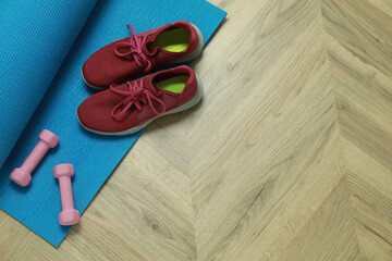 Dumbbells, sneakers and mat on wooden floor, above view. Space for text