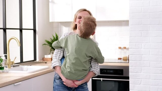 Excited mom or babysiter and kid boy jumping, dancing, laughing in modern scandinavian house kitchen. Happy family mother and son having fun enjoy playing singing together at home