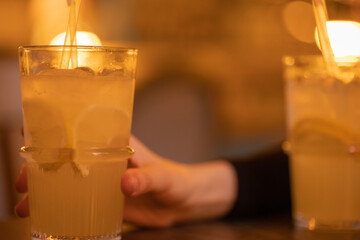 A glass with lemonade, lemon wedges, ice cubes. Summer cold refreshing drink, alcoholic cocktail in the hand of a man on the table in a bar. Close-up