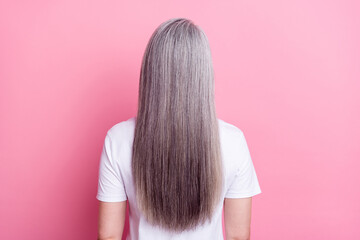 Back view photo portrait of senior woman with long straight grey hair isolated on pastel pink color background