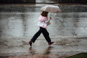 a girl with an umbrella runs through puddles in the rain. wet feet and clothes during a heavy rainstorm. a man escapes from the weather